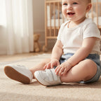 Smiling baby wearing white first walker shoes while sitting on a soft rug