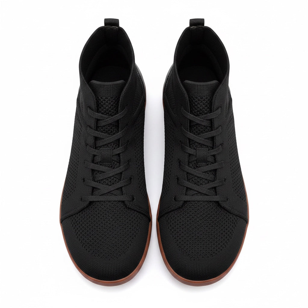 A pair of black lace up ankle sneakers with a perforated upper and brown rubber soles, shown from a top-down view. 
