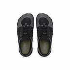 A pair of minimalist slip on shoes shown from a top down view. The shoes feature a black and dark grey knit upper with a textured sole, black laces, and a muted olive green interior lining.