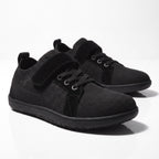 A pair of black low top Children's barefoot shoes with a knit mesh upper, black laces, and hook and-loop strap closures.