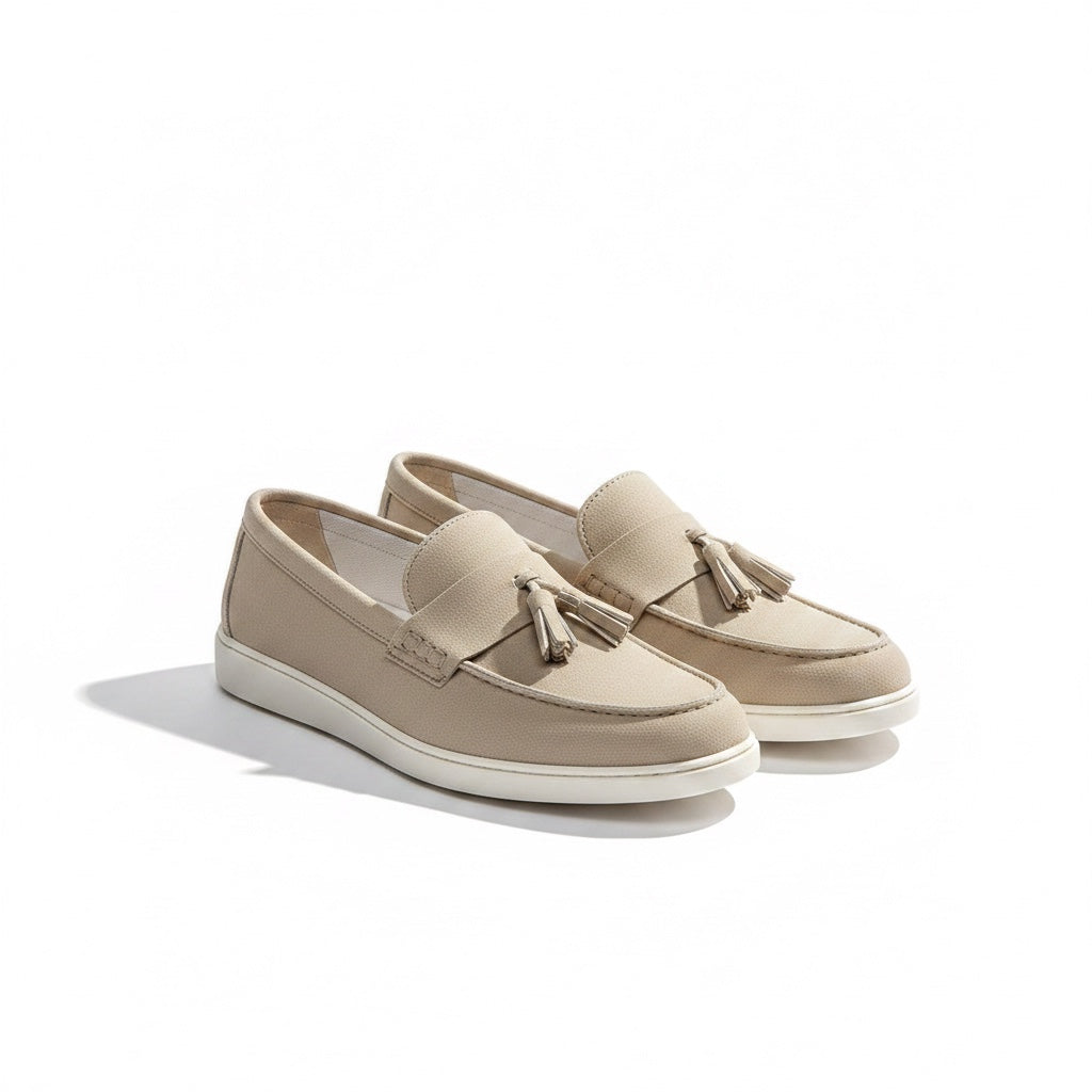 A pair of beige slip on loafers with tassel details and white soles.