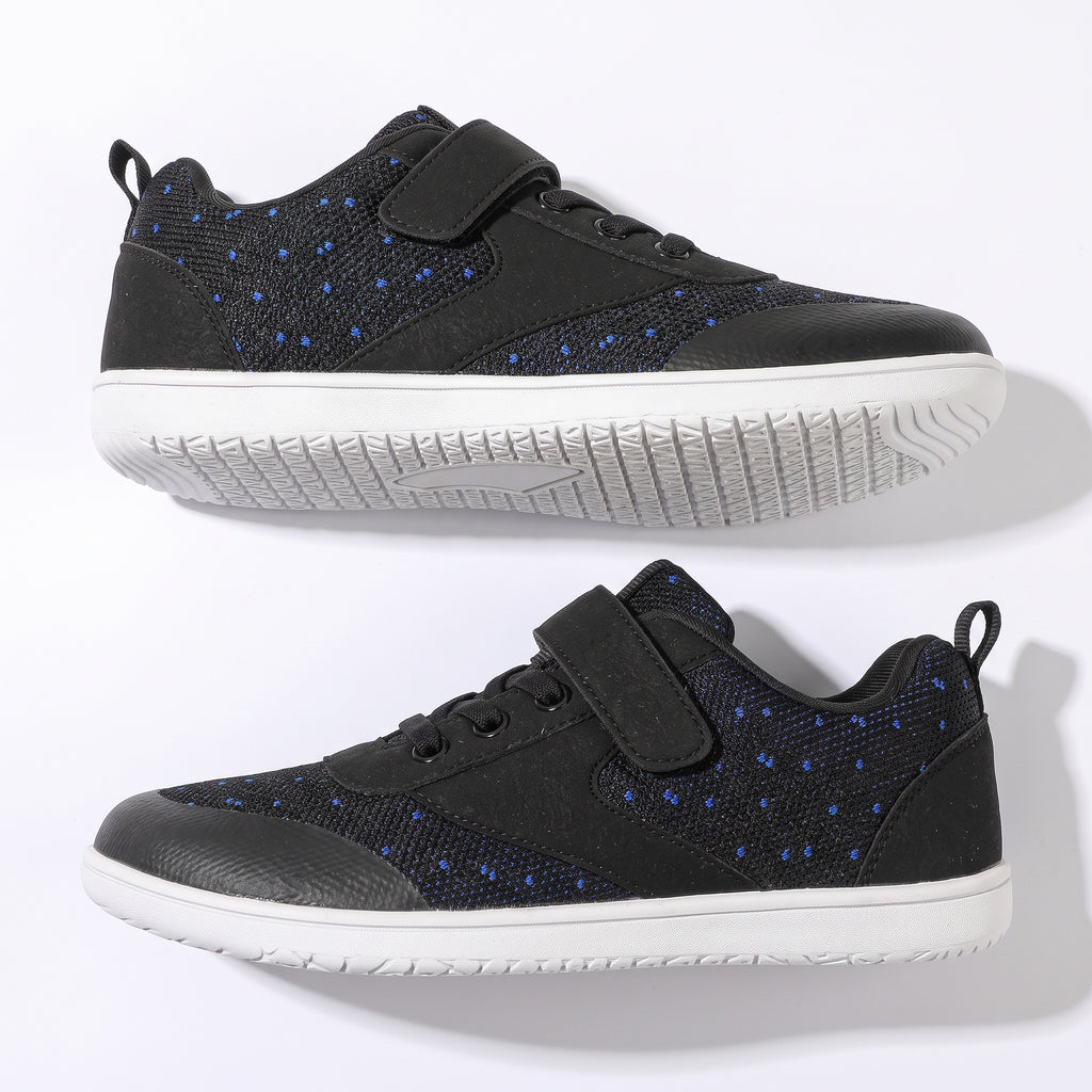A pair of black low top children's barefoot shoes with blue dotted pattern panels, featuring hook-and-loop strap closures and white soles