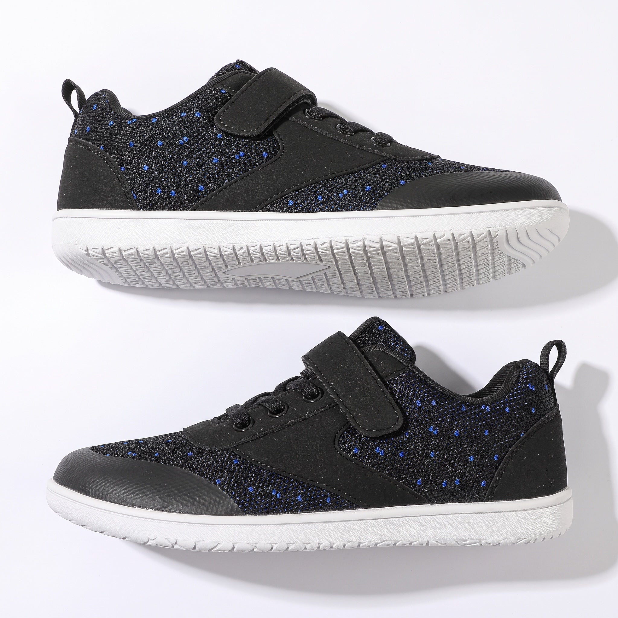A pair of black low top children's barefoot shoes with blue dotted pattern panels, featuring hook-and-loop strap closures and white soles