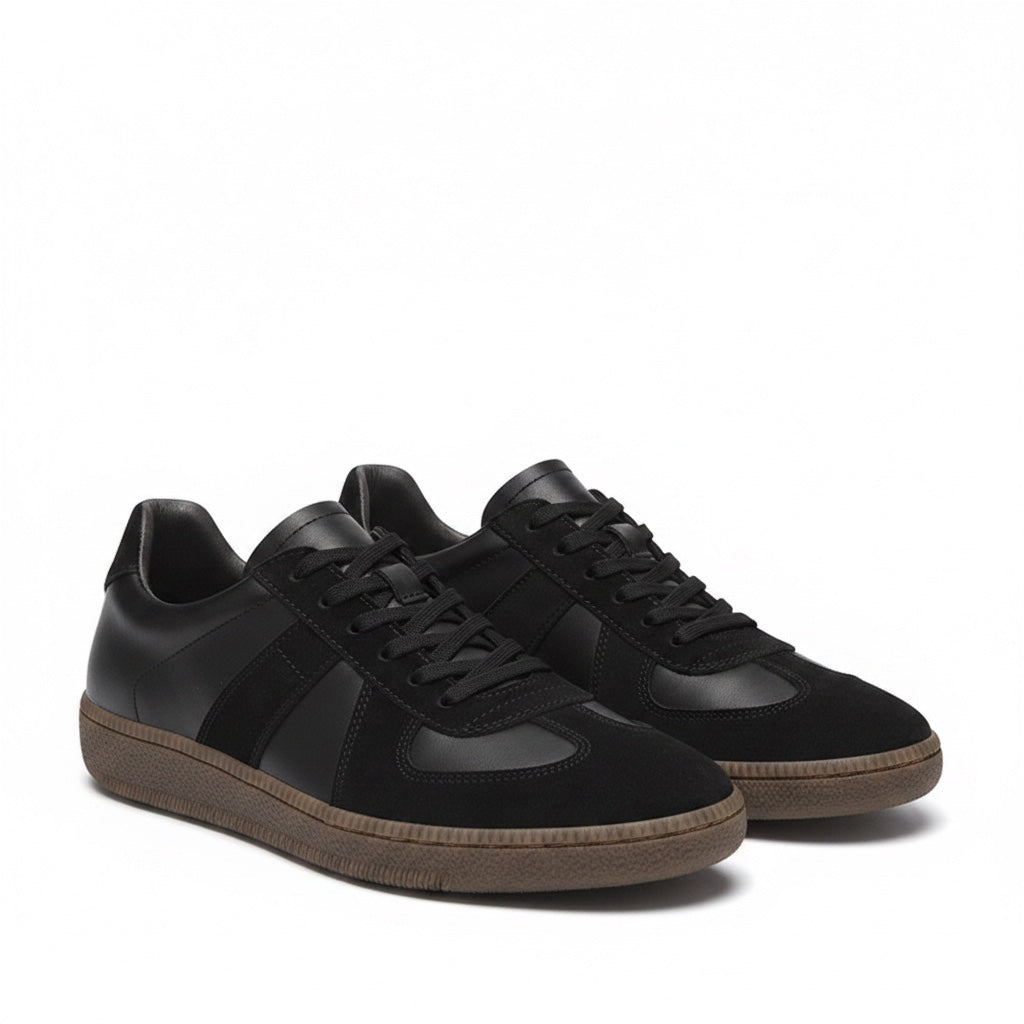 A pair of black leather and suede low top sneakers with black laces and brown gum soles
