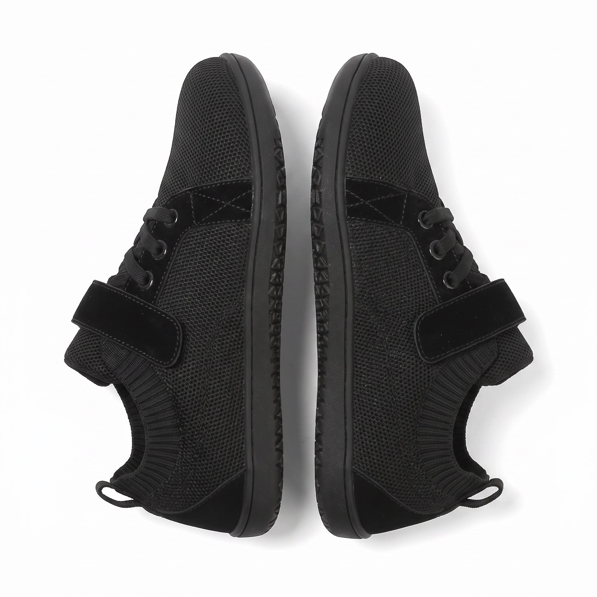 A pair of black low top barefoot shoes  shown from a top down view on a white background. The shoes feature a textured knit upper, black laces, a hook and loop strap across the instep.