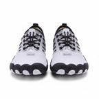 A pair of minimalist athletic sneakers shown from the front on a clean white background. The shoes feature a white mesh upper with black laces, black heel accents, and a black and white wavy sole.