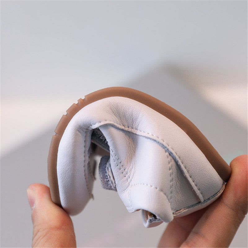 White baby shoe being gently bent to demonstrate its flexible construction