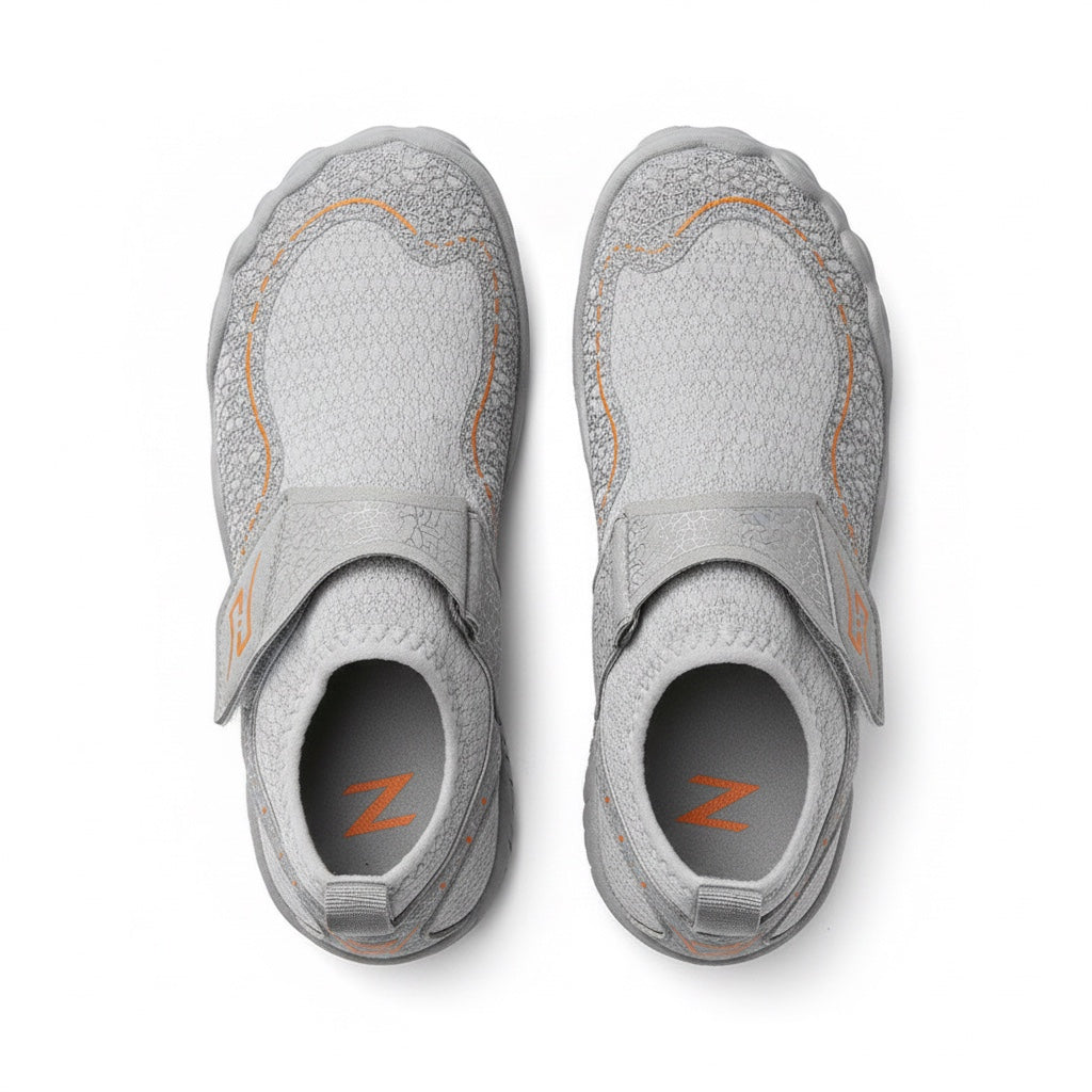 A pair of light grey Children's  slip on shoes with orange accents and a hook and loop strap, shown from a top down view.