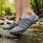 Person wearing gray barefoot water shoes while walking through a shallow outdoor stream
