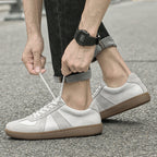 Person tying the laces of white  Loafers with brown soles on a street.
