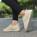 Person wearing beige knit barefoot shoes outdoors on a paved path, showing the flexible casual design.