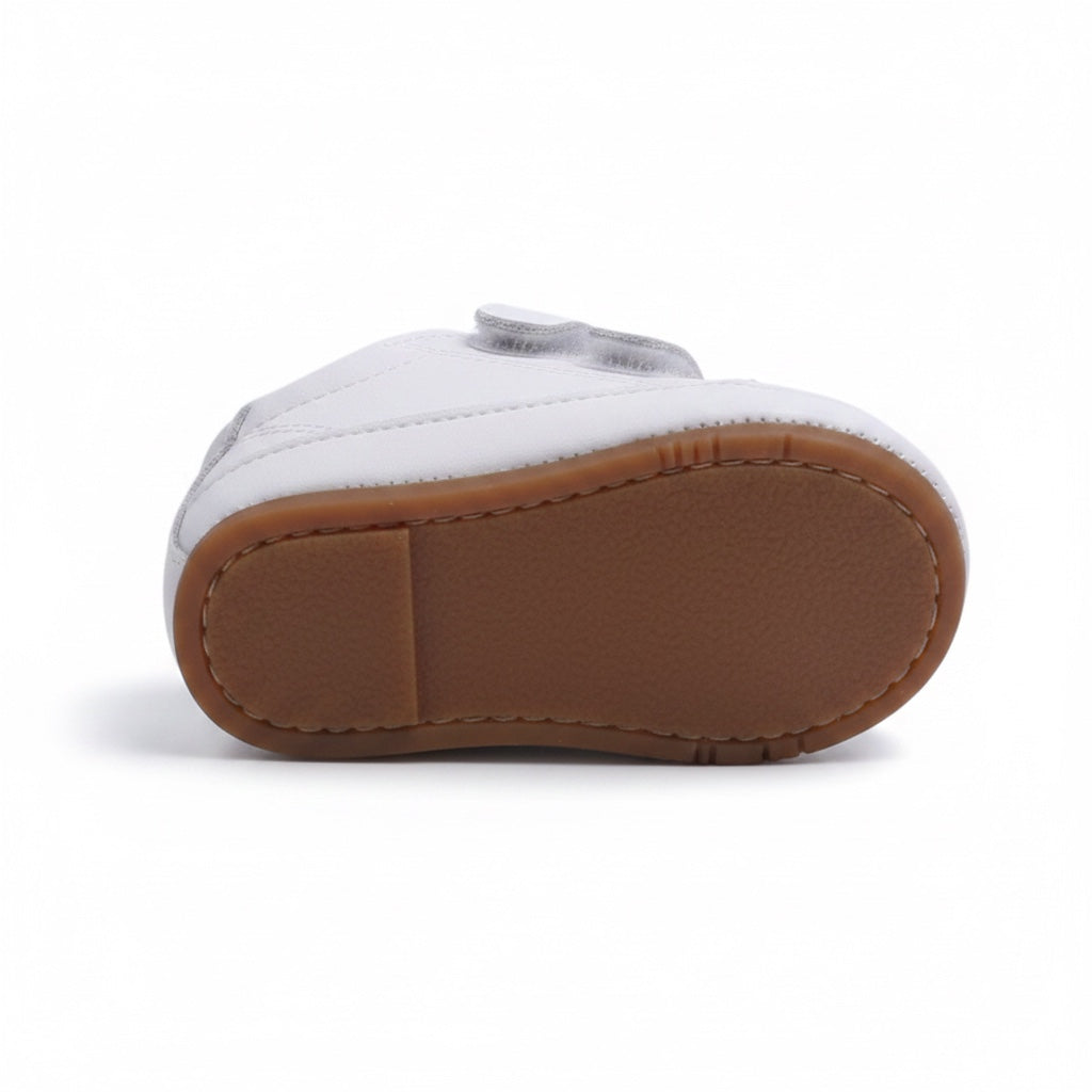 Bottom view of a white baby shoe showing its brown flexible rubber sole
