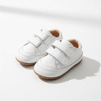 Pair of white baby shoes displayed in natural light with their flexible design visible