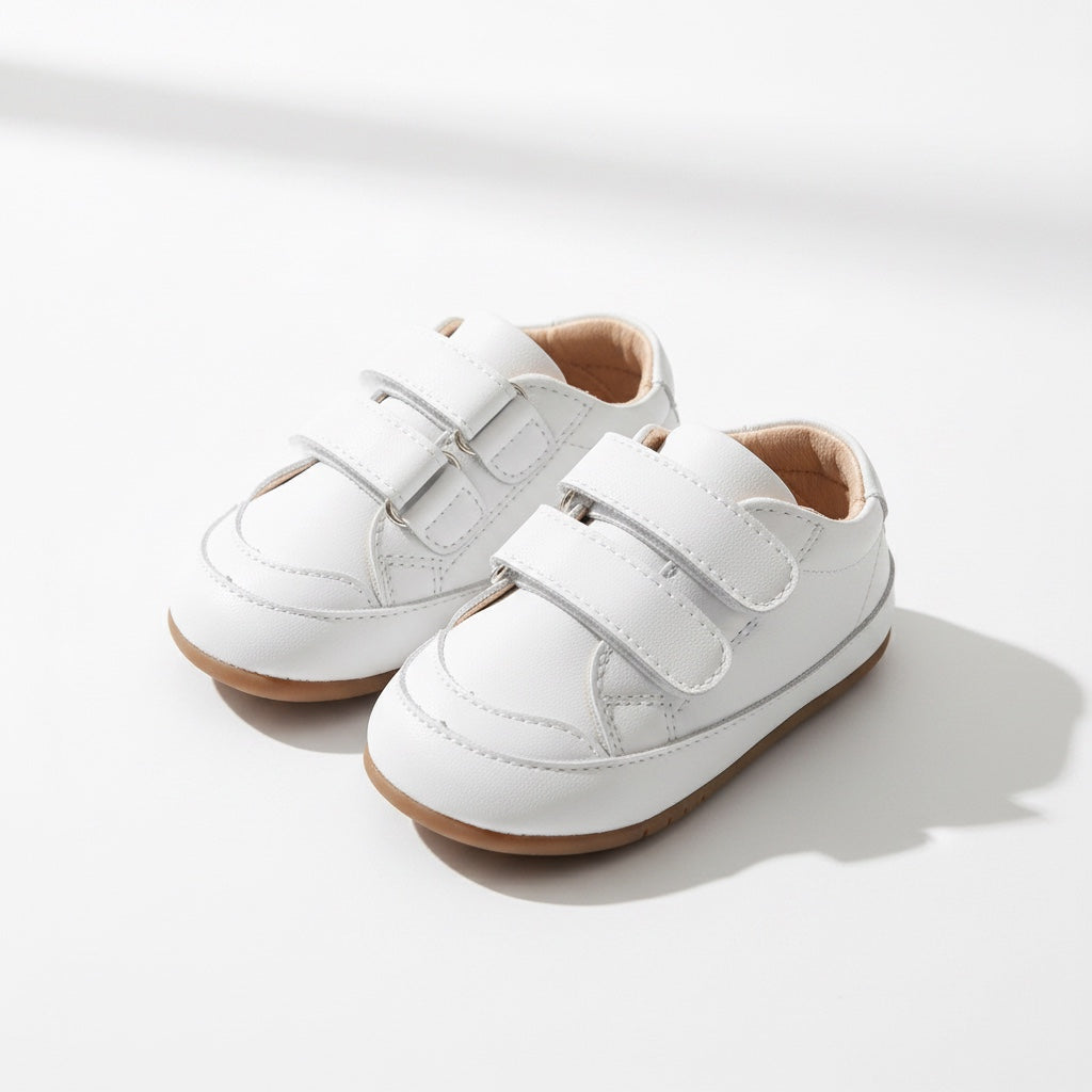 Pair of white baby shoes displayed in natural light with their flexible design visible